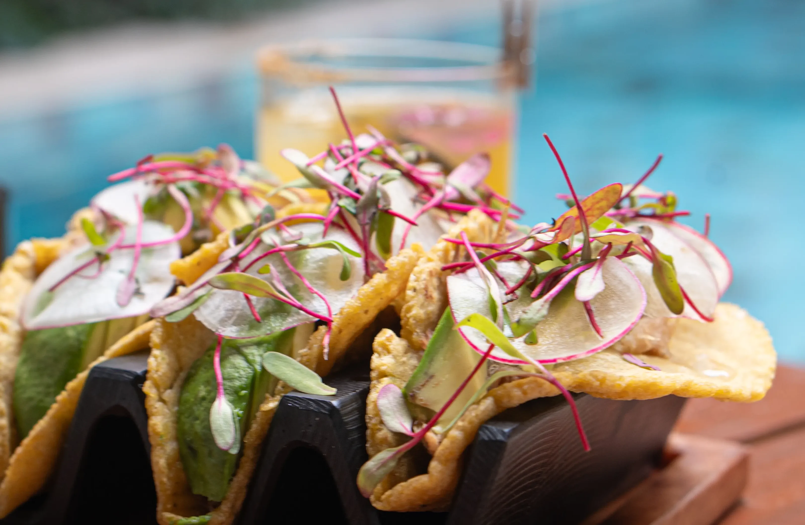 Tacos with avocado and microgreens near pool.