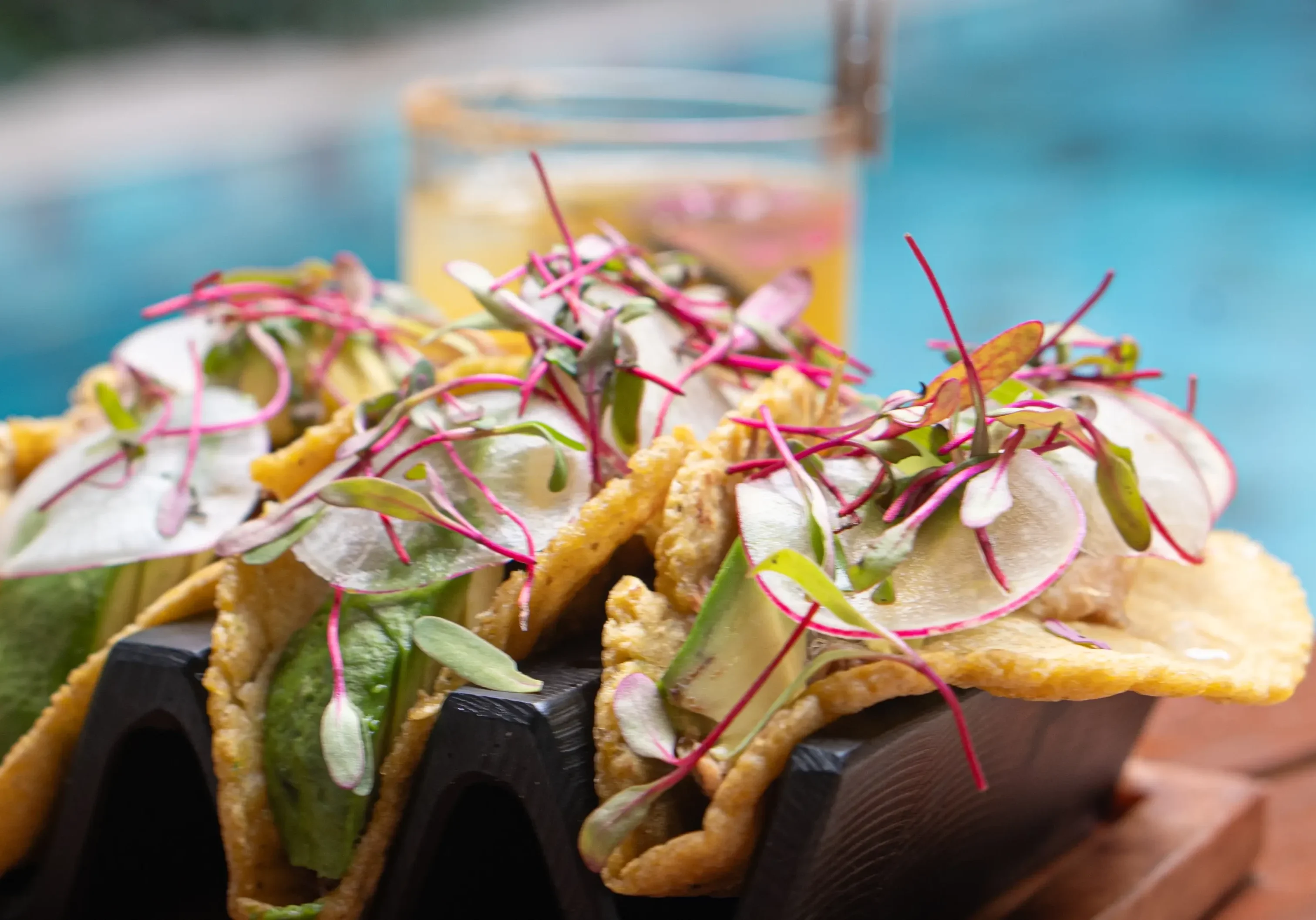 Tacos with avocado and microgreens near pool.